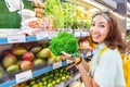 asian woman choosing broccoli and other vegetables in supermarket