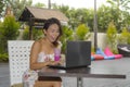 Happy Asian woman in elegant and dress sitting outdoors at pool resort coffee shop having healthy fruit juice working on lapt Royalty Free Stock Photo