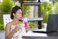Happy Asian woman in elegant and dress sitting outdoors at pool resort coffee shop having healthy fruit juice working on lapt Royalty Free Stock Photo