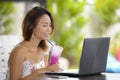 Happy Asian woman in elegant and dress sitting outdoors at pool resort coffee shop having healthy fruit juice working on lapt Royalty Free Stock Photo