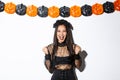 Happy asian woman enjoying halloween, wearing wicked witch costume and rejoicing against pumpkin streamers decoration