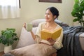 A happy Asian woman is enjoying her morning coffee and reading a book in her bedroom Royalty Free Stock Photo