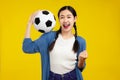 Happy Asian woman football fan cheer up support favorite team with soccer ball isolated on yellow background. People emotions Royalty Free Stock Photo