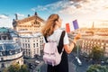 Asian woman with french flag and backpack standing on a roof top and enjoys great view over Parisian skyline at sunset.