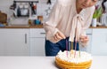 Happy Asian woman lights candles on a birthday cake. Close-up. Royalty Free Stock Photo