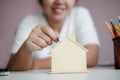 Happy Asian woman putting money coin to the wooden house piggy bank metaphor saving money for buy the house select focus shallow Royalty Free Stock Photo