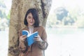 Happy asian woman reading book outdoor in green park nature. Reading book magazine relaxation woman. Leisure portrait woman smile