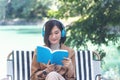 Happy asian woman reading book use headphones listen to music outdoor in green park nature. Reading book magazine, Music therapist Royalty Free Stock Photo