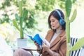 Happy asian woman reading book use headphones listen to music outdoor in green park nature. Reading book magazine, Music therapist Royalty Free Stock Photo