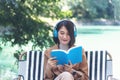 Happy asian woman reading book use headphones listen to music outdoor in green park nature. Reading book magazine, Music therapist Royalty Free Stock Photo