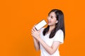 Happy Asian woman 20s singing while holding smartphone like microphone and listening to music via earphones isolated over backgrou Royalty Free Stock Photo