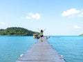 Happy Asian woman short hair raise up her hands with relaxation while walking on the wooden bridge to the boat pier on sea. Royalty Free Stock Photo