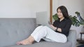 Happy asian woman sitting on couch and surfing internet, reading news on her laptop computer Royalty Free Stock Photo