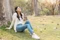 happy Asian woman sitting on grass in the green park, relaxing with nature in the park Royalty Free Stock Photo