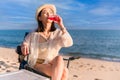 Happy Asian woman sitting on picnic chair holding red water bottle and drinking for refresh while camping travel trip on beach in