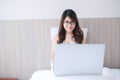 Happy asian woman sitting and using computer laptop on white bed. Young adult female smiling and cheerful during Working from home Royalty Free Stock Photo