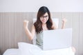 Happy asian woman sitting and using computer laptop on white bed. Young adult female smiling and cheerful during Working from home Royalty Free Stock Photo