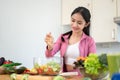 A happy Asian woman is squeezing a lemon on her salad, making her healthy breakfast in the kitchen Royalty Free Stock Photo