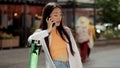 Happy asian woman stands with modern electric scooter talking on phone in city street. Pretty girl riding an electric Royalty Free Stock Photo