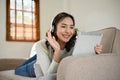 Happy Asian woman talking with her friends on a video call on tablet while laying on sofa Royalty Free Stock Photo