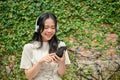 A happy Asian woman is texting with her friends and listening to music while relaxing on a bench Royalty Free Stock Photo