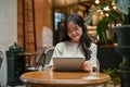 A happy Asian woman is using her tablet while relaxing at a beautiful coffee shop in the city Royalty Free Stock Photo