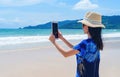 Happy Asian woman using mobile phone to take a photo by camera on social media at beach during travel holidays vacation outdoors Royalty Free Stock Photo