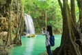 Happy Asian woman using mobile phone to take a photo by camera on social media at Erawan waterfall in tropical forest with trees Royalty Free Stock Photo