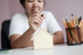 Happy Asian woman using pencil draw and plan with wooden house piggy bank metaphor planning to saving money for buy the house Royalty Free Stock Photo