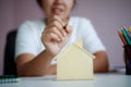 Happy Asian woman using pencil draw and plan with wooden house piggy bank metaphor planning to saving money for buy the house Royalty Free Stock Photo