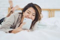 Happy Asian women are using smart phone on the bed in morning. Asian woman in bed checking social apps with smartphone. Royalty Free Stock Photo