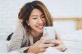 Happy Asian women are using smart phone on the bed in morning. Asian woman in bed checking social apps with smartphone. Royalty Free Stock Photo