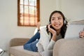 Happy Asian woman wearing headphones, listening to music while laying on sofa in living room Royalty Free Stock Photo