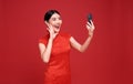 Happy Asian woman wearing traditional cheongsam qipao dress having video-call with lover holding smart phone in hand shooting