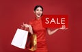 Happy Asian woman wearing traditional cheongsam qipao dress holding sale sign and shopping bag isolated on red background. Happy Royalty Free Stock Photo