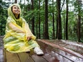 Happy Asian woman wearing yellow raincoat sit on wooden floor under rain Royalty Free Stock Photo