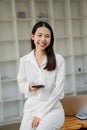 A happy Asian woman in a white dress uses her smartphone to check email or social media on the Internet. Royalty Free Stock Photo