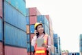 Happy Asian woman worker with helmet and safety vest using digital tablet and walkie talkie during inspection at logistic shipping Royalty Free Stock Photo