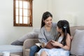 happy asian woman reading a book to daughter embracing her at home. sitting on sofa Royalty Free Stock Photo