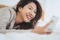 Happy Asian women are using smart phone on the bed in morning. Asian woman in bed checking social apps with smartphone. Royalty Free Stock Photo