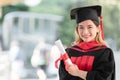 Happy Asian young beautiful graduate female student with University degree standing and holding diploma in hand after graduation Royalty Free Stock Photo