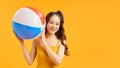 Happy Asian young beautiful woman holding beach ball in summer holiday travel isolated studio shot on yellow background Royalty Free Stock Photo