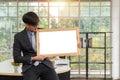 Happy Asian young businessman holding an empty white board and sitting on the table in office. Concept of copy space for advertise Royalty Free Stock Photo