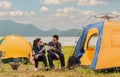 Happy Asian young couple sitting on picnic chair drinking tea and coffee while tent camp lakeside at parks outdoors on vacation