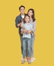 Happy Asian young family with one child standing embracing and smiling at camera isolated on yellow Royalty Free Stock Photo