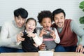 Happy Asian young gay couple and multiethnic adopted kids wearing sweater holding joysticks enjoy playing game with excited face Royalty Free Stock Photo