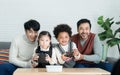 Happy Asian young gay couple and multiethnic adopted kids wearing sweater holding joysticks enjoy playing game with excited face Royalty Free Stock Photo