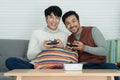 Happy Asian young gay couple wearing sweater holding joysticks enjoy playing game and have fun together at living room at home. Royalty Free Stock Photo