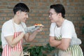 Happy Asian young LGBT gay couple making pizza together. Handsome man showing sliced homemade pizza to his boyfriend for smell