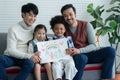Happy Asian young LGBTQ gay couple with little cute adopted Caucasian and African kid smiling and showing rainbow family drawing Royalty Free Stock Photo